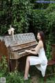 A woman in a white dress sitting on a bench next to a piano.