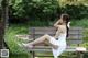 A woman in a white dress sitting on a wooden bench.