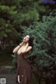 A woman in a brown dress standing in front of a tree.