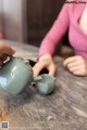 A woman pouring tea into a teapot on a table.