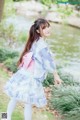 A woman in a blue and pink kimono standing next to a pond.