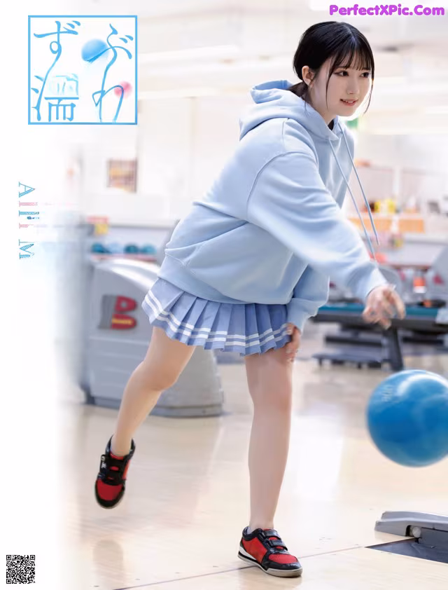 A woman in a blue sweatshirt and skirt is playing with a blue ball.