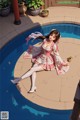 A woman in a pink dress sitting on the edge of a pool.