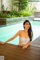 A woman in a white lingerie sitting by a swimming pool.