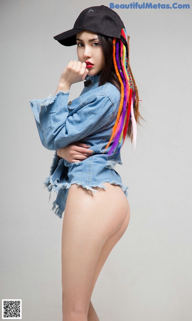 A woman with colorful hair wearing a denim jacket and a baseball cap.