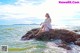 A woman sitting on a rock in the ocean.