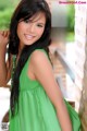 A woman in a green dress leaning against a brick wall.