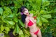 A woman in a red bikini posing in front of a bush.