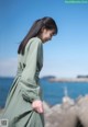 A woman in a green dress standing on a rock by the ocean.