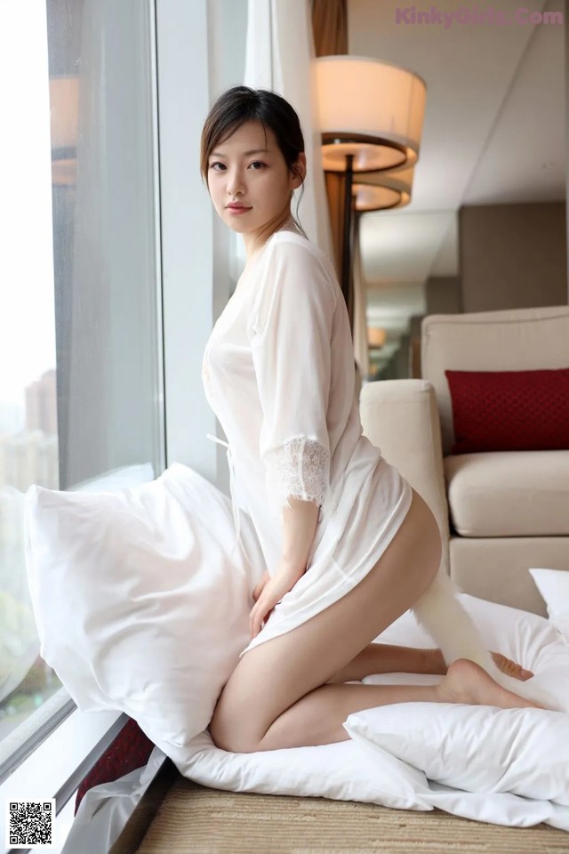 A woman in a white robe sitting on a bed.