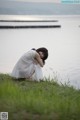 A woman in a white dress sitting on the grass by the water.