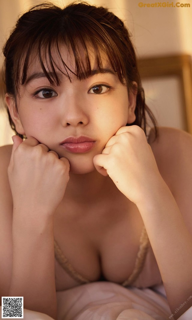 A woman laying on top of a bed with her hand on her chin.