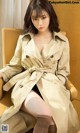 A woman in a trench coat sitting on a chair.