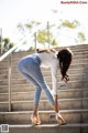 A woman in a white shirt and blue jeans is bending over on some steps.