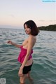 A woman in a pink top and black shorts standing in the water.