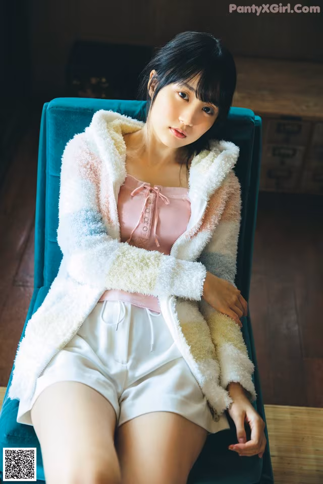 A woman sitting on a blue chair wearing white shorts and a pink top.