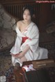 A woman in a white and red kimono sitting on a rug.