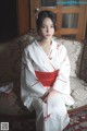 A woman in a white and red kimono sitting on a couch.