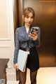 a woman in a blue shirt and black skirt holding a cell phone