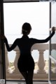 A woman standing in front of a window looking out at the ocean.